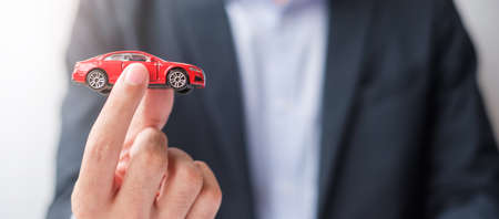 Businessman hand holding red car toy. Car insurance, warranty, rental, Financial, new and repair conceptの写真素材