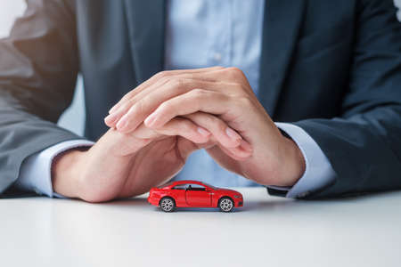 Businessman hand cover or protection red car toy on table. Car insurance, warranty, repair, Financial, banking and money conceptの写真素材
