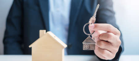 Businessman hand holding key with wooden Home model. Real estate, buy and sale, Property insurance, rental and contract agreement conceptsの写真素材