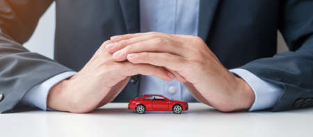 Businessman hand cover or protection red car toy on table. Car insurance, warranty, repair, Financial, banking and money conceptの写真素材