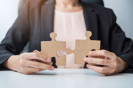 Woman connecting couple puzzle piece, wood jigsaw on table. Business solutions, mission, success,...