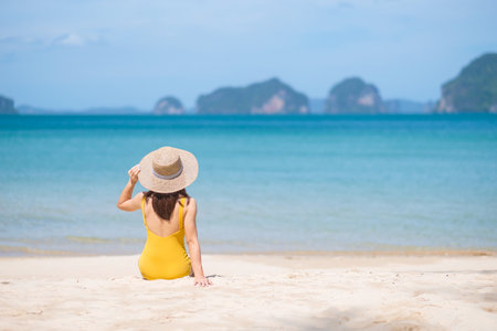 Woman tourist in yellow swimsuit and hat, happy traveler sunbathing at Paradise beach on Islands. destination, wanderlust, Asia Travel, tropical summer, vacation and holiday conceptの写真素材