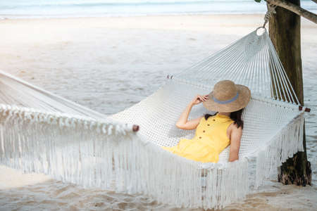 Happy Woman Traveler is relaxing in a hammock on the paradise beach. Female tourist in yellow dress rest near tropical sea. vacation, travel, summer, Wanderlust and holiday conceptの写真素材