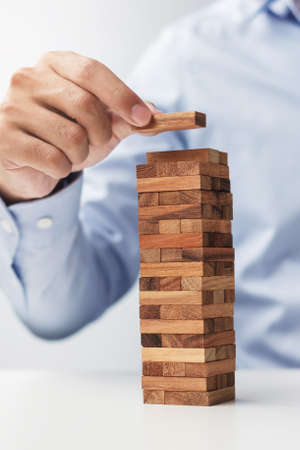 Businessman hand placing or pulling wooden block on the tower. Business planning, Risk Management, Solution and strategy Conceptsの写真素材