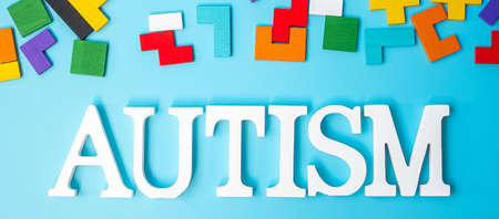 AUTISM text with colorful wood puzzle pieces, geometric shape block on blue background. Concepts of health, Autistic Spectrum disorder and world Autism awareness dayの写真素材