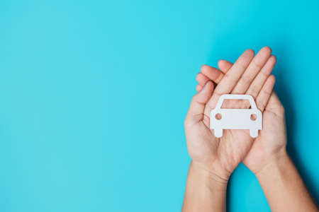 Hand holding paper Car cutout on blue background. Vehicle insurance, warranty, Automobile rental, Transportation, Maintenance and repair concept.の写真素材
