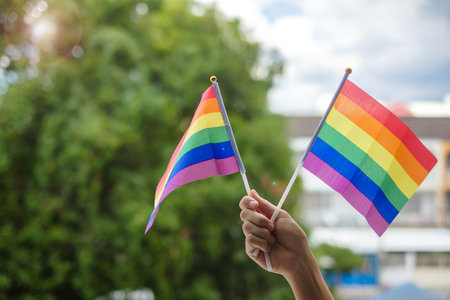 hands showing LGBTQ Rainbow flag on green nature background. Support Lesbian, Gay, Bisexual,...