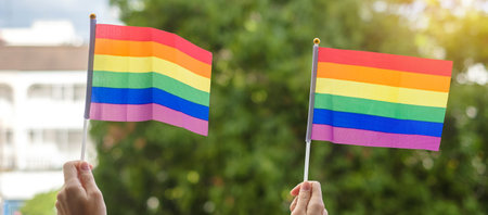 hands showing LGBTQ Rainbow flag on green nature background. Support Lesbian, Gay, Bisexual,...