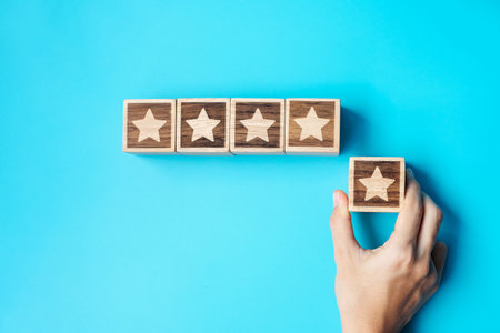 hand holding Star block on blue background. Customer choose rating for user reviews. Service rating, ranking, customer review, satisfaction, evaluation and feedback conceptの写真素材