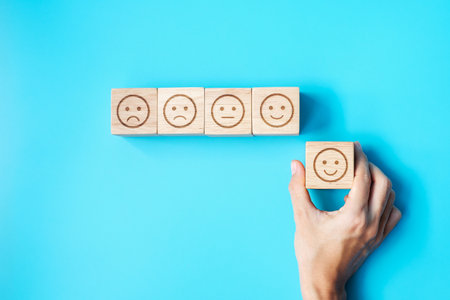 Man hand holding emotion face block. Customer choose Emoticon for user reviews. Service rating, ranking, customer review, satisfaction, evaluation and feedback conceptの写真素材