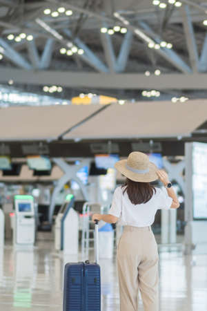 Young woman hand holding luggage handle before checking flight time in airport, Transport, insurance, travel and vacation conceptsの写真素材