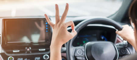 woman showing OK sign during driving a car on the road, hand controlling steering wheel in electric modern automobile. Journey, trip and safety Transportation conceptsの写真素材