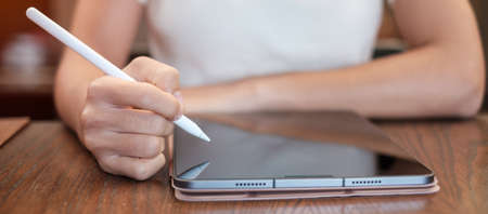 woman using tablet for sms messages, hand holding pencil typing touchscreen mobile phone in cafe or...