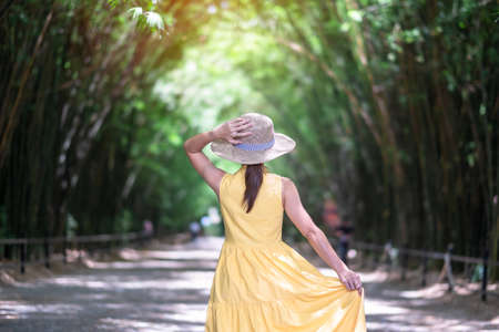 Asian Woman in yellow dress and hat Traveling at green Bamboo Tunnel, Happy traveler walking Chulabhorn wanaram temple. landmark and popular for tourists attractions in Nakhon Nayok, Thailandの写真素材