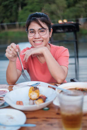 Happy woman eating dinner with delicious grilled meat and BBQ in outdoor. Barbecue, Party, lifestyle and picnic conceptの写真素材