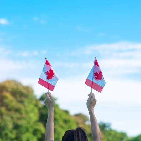 hand holding Canada flag on blue sky background. Canada Day  and happy celebration conceptsの写真素材