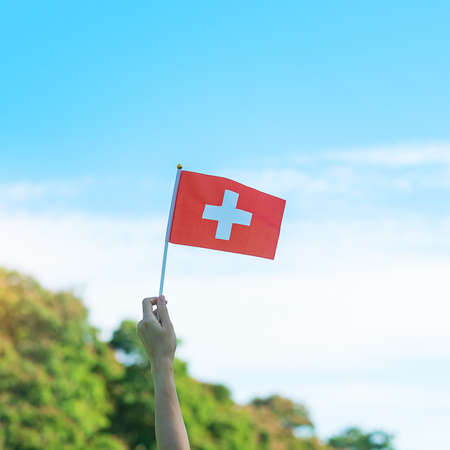 hand holding Switzerland flag on blue sky background. Switzerland National Day and happy celebration conceptsの写真素材