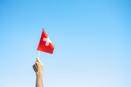 hand holding Switzerland flag on blue sky background. Switzerland National Day and happy celebration conceptsの写真素材