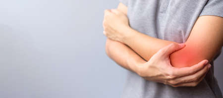 adult female with her muscle pain on gray background. Woman having elbow ache due to lateral...