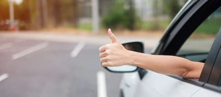 woman hand Thumb up during driving a car on the road, hand controlling steering wheel in electric...