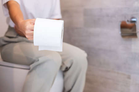 Woman holding toilet paper roll during sit on toilet bowl. diarrhea, constipated period, infection, abdominal, stomachache, cystitis, Insurance and Medical conceptの写真素材