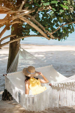 Happy Woman Traveler is relaxing in a hammock on the paradise beach. Female tourist in yellow dress rest near tropical sea. vacation, travel, summer, Wanderlust and holiday conceptの写真素材