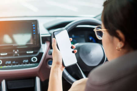 Woman hand holding smartphone while driving car. Dangerous, Journey, trip and Transportation conceptsの写真素材
