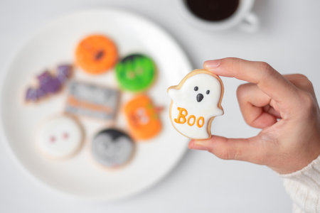 woman hand holding funny Halloween Cookie during drinking coffee. Happy Halloween day, Trick or Threat, Hello October, fall autumn, Traditional, party and holiday conceptの写真素材