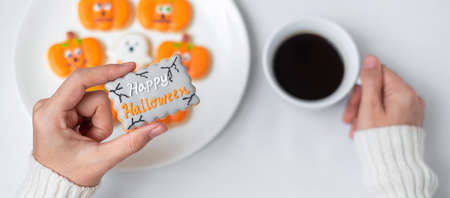 woman hand holding funny Halloween Cookie during drinking coffee. Happy Halloween day, Trick or Threat, Hello October, fall autumn, Traditional, party and holiday conceptの写真素材