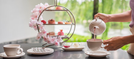 Woman hand pouring hot tea with Afternoon tea set and Pink dessert at luxury hotelの写真素材