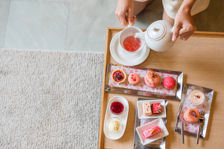 Woman hand pouring hot tea with Afternoon tea set and Pink dessert at luxury hotelの写真素材