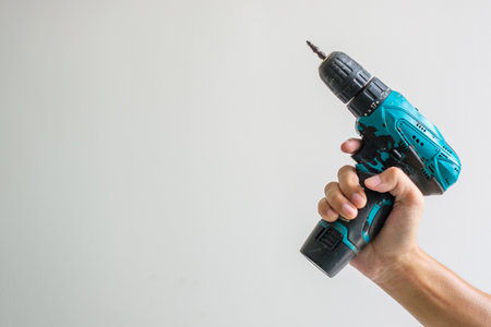man hand holding cordless screwdriver with wall background, Carpenter working with electric screwdriver on the workの写真素材