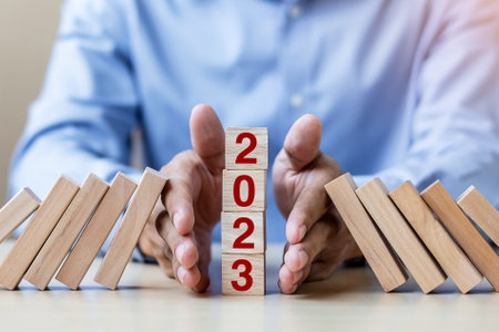 Businessman hand Stopping Falling of 2023 wooden Blocks. Business, Risk Management, Insurance, Resolution, strategy, solution, goal, New Year New You and happy holiday conceptsの写真素材
