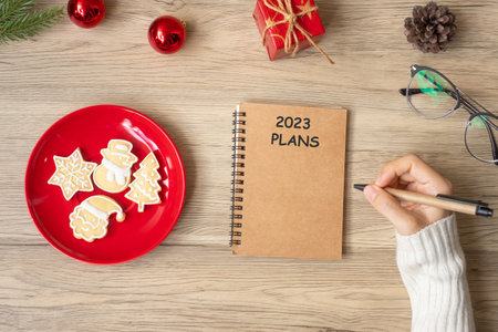 Woman hand writing 2023 PLANS on notebook with Christmas cookies on table. Xmas, Happy New Year, Goals, Resolution, To do list, and Strategy conceptの写真素材
