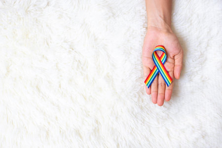 hand showing LGBTQ Rainbow ribbon on white bed background. Support Lesbian, Gay, Bisexual, Transgender, Queer community and Rights conceptの写真素材