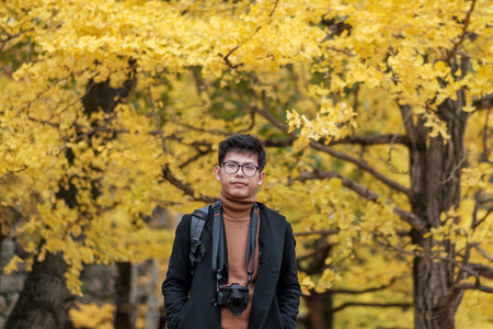Happy man enjoy at the park outdoor in Autumn season, Asian traveler in coat and camera against Yellow Ginkgo Leaves backgroundの写真素材