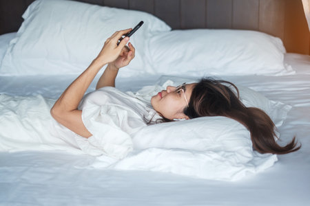 woman using smartphone for social media, young female watching movies by mobile phone on bed at home. technology, network, online shopping, e commerce, lifestyle and digital communication conceptの写真素材