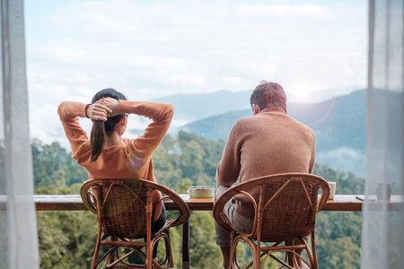 Couple tourist drinking coffee and eating breakfast against mountain view at countryside home or homestay in the morning. Vacation, together travel, honeymoon, blogger, journey and trip conceptの写真素材