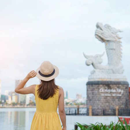 Woman Traveler with yellow dress visiting in Da Nang. Tourist sightseeing the river view with Carp Dragon Statue or Ca Chep Hoa Rong.Landmark and popular. Vietnam and Southeast Asia travel conceptの写真素材