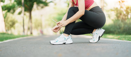Young athlete woman tying running shoes in the park outdoor, female runner ready for jogging on the road outside, asian Fitness walking and exercise on footpath in morning. wellness and sport conceptsの写真素材