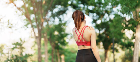 Young fitness woman holding her sports injury shoulder and neck, muscle painful during training. Asian runner female having body problem after exercise outside in summerの写真素材