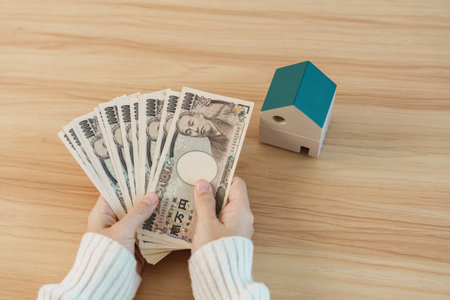 Woman holding Japanese Yen banknote and House model. Real Estate, Home, Mortgage, Japan cash, Tax, Recession Economy, Inflation, Investment, finance and savings conceptsの写真素材