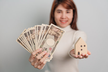 Woman holding Japanese Yen banknote and House model. Real Estate, Home, Mortgage, Japan cash, Tax, Recession Economy, Inflation, Investment, finance and savings conceptsの写真素材
