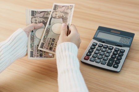 Woman hand counting Japanese Yen banknote with calculator. Thousand Yen money. Japan cash, Tax, Recession Economy, Inflation, Investment, finance, savings, salary and payment conceptsの写真素材