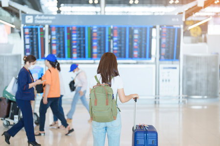 Young woman with bag and luggage looking to flight time information board in international airport, before check in. Travel, Vacation, trip and Transport conceptの写真素材