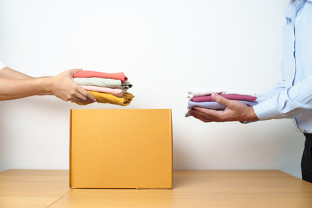 Donation, Charity, Volunteer, Giving, Delivery and Home Moving Concept. Hand holding Clothes into cardboard box at home for support and help poor, refugee and homeless people. Copy space for textの写真素材