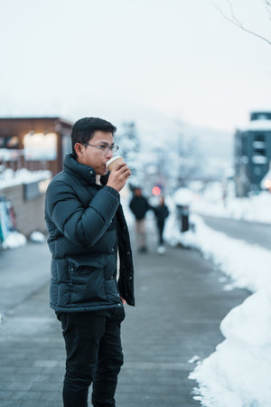 man tourist holding hot Coffee or Tea paper cup with snow in winter season during travel in Niseko. landmark and popular for attractions in Hokkaido, Japan. Travel and Vacation conceptsの写真素材