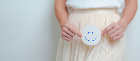 Woman hold Good and happy Face paper over abdomen. Ovarian and Cervical cancer, Endometriosis, Hysterectomy, Uterine, Reproductive, menstruation, Infertility, Pregnancy and Sexual Transmitted diseaseの写真素材