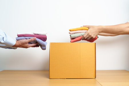 Donation, Charity, Volunteer, Giving, Delivery and Home Moving Concept. Hand holding Clothes into cardboard box at home for support and help poor, refugee and homeless people. Copy space for textの写真素材