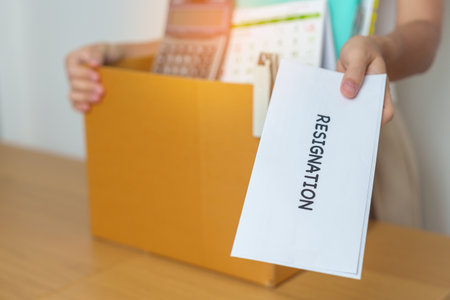 Resignation, Layoff, Unemployment, Dismiss, Job quit, Jobless and Farewell concept. Businesswoman holding letter of Resign contract with documents cardboard box at officeの写真素材